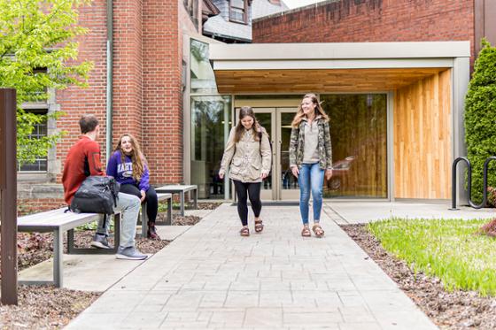 Photo of two Chatham University students walking on Shadyside Campus, with two other students seated nearby on a bench